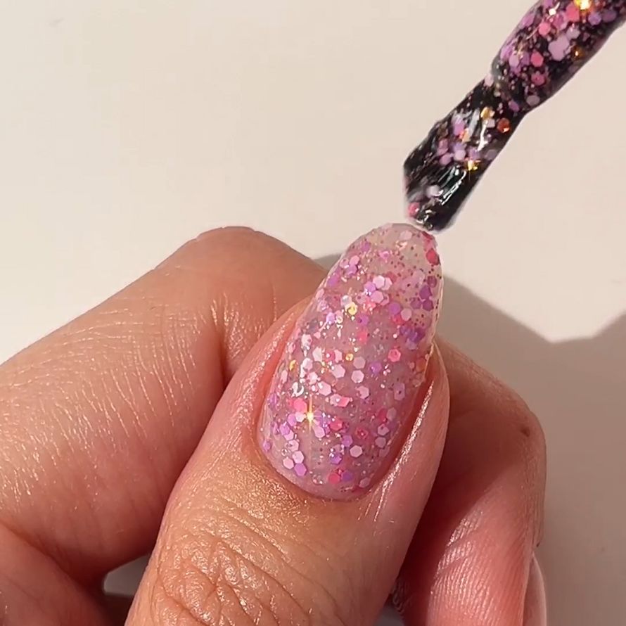 Nail polish is applied to a nail with pink glitter.