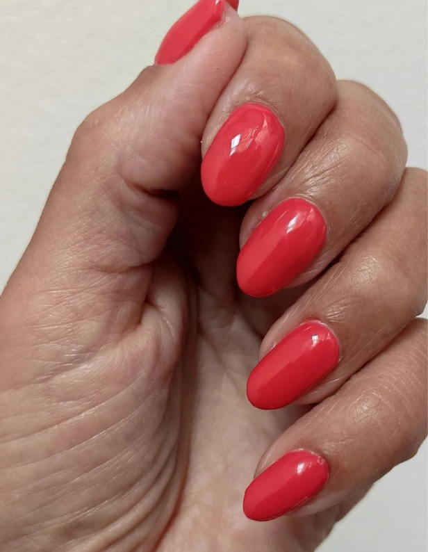 Hand holding bright red nail polish on short-cut nails.