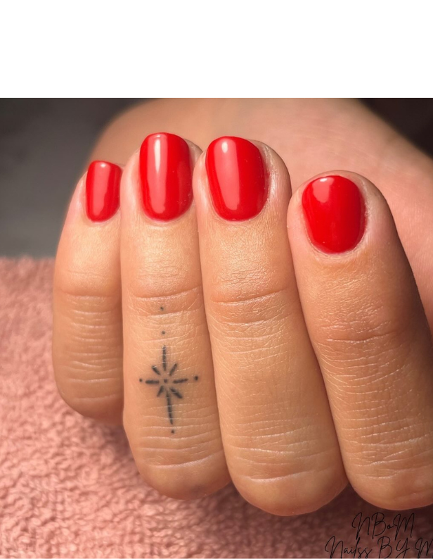 Red painted nails on one hand, with a small star-shaped tattoo on the middle finger, resting on a pink towel.
