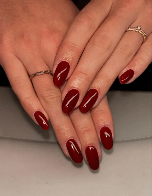 Hands with long, dark red nails and rings on a few fingers.