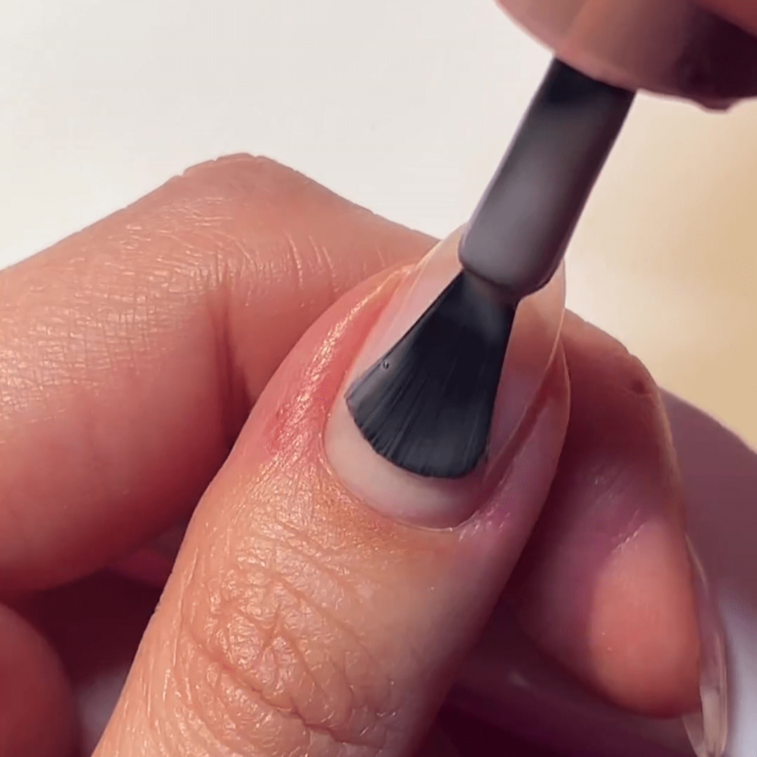 Close-up of a hand on which a transparent varnish is applied to a fingernail with a brush.
