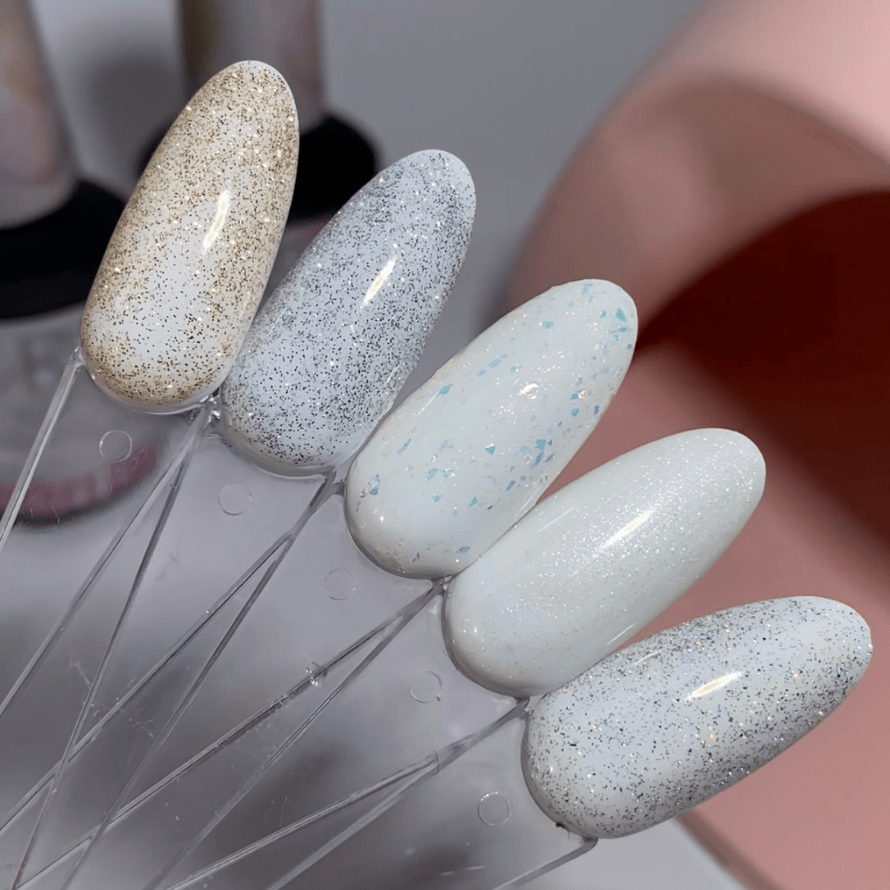 Five nail art examples on sticks, with various white and glitter designs in gold, silver and bluish tones.