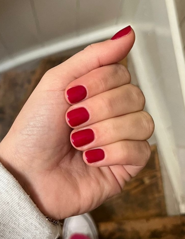 A hand with short-cut nails, painted in a shiny red color.