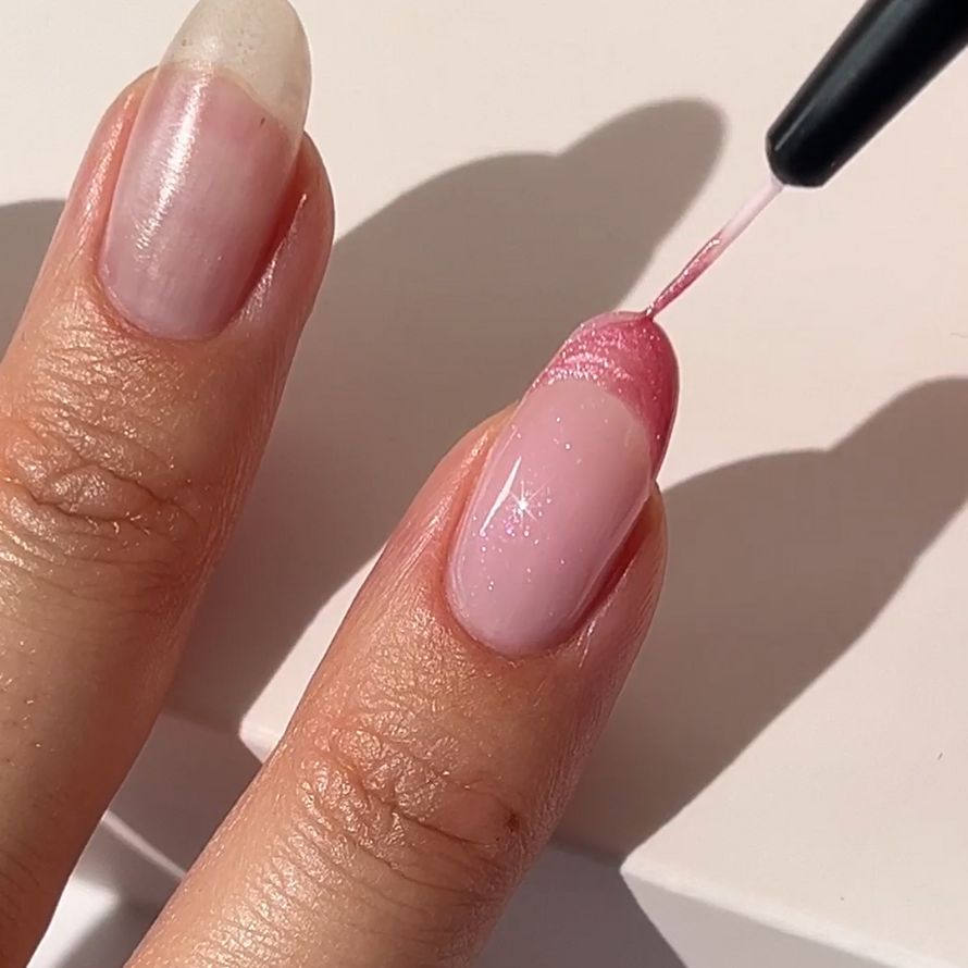 Close-up of a hand with manicure. One nail is painted with a pink, glittering nail polish.