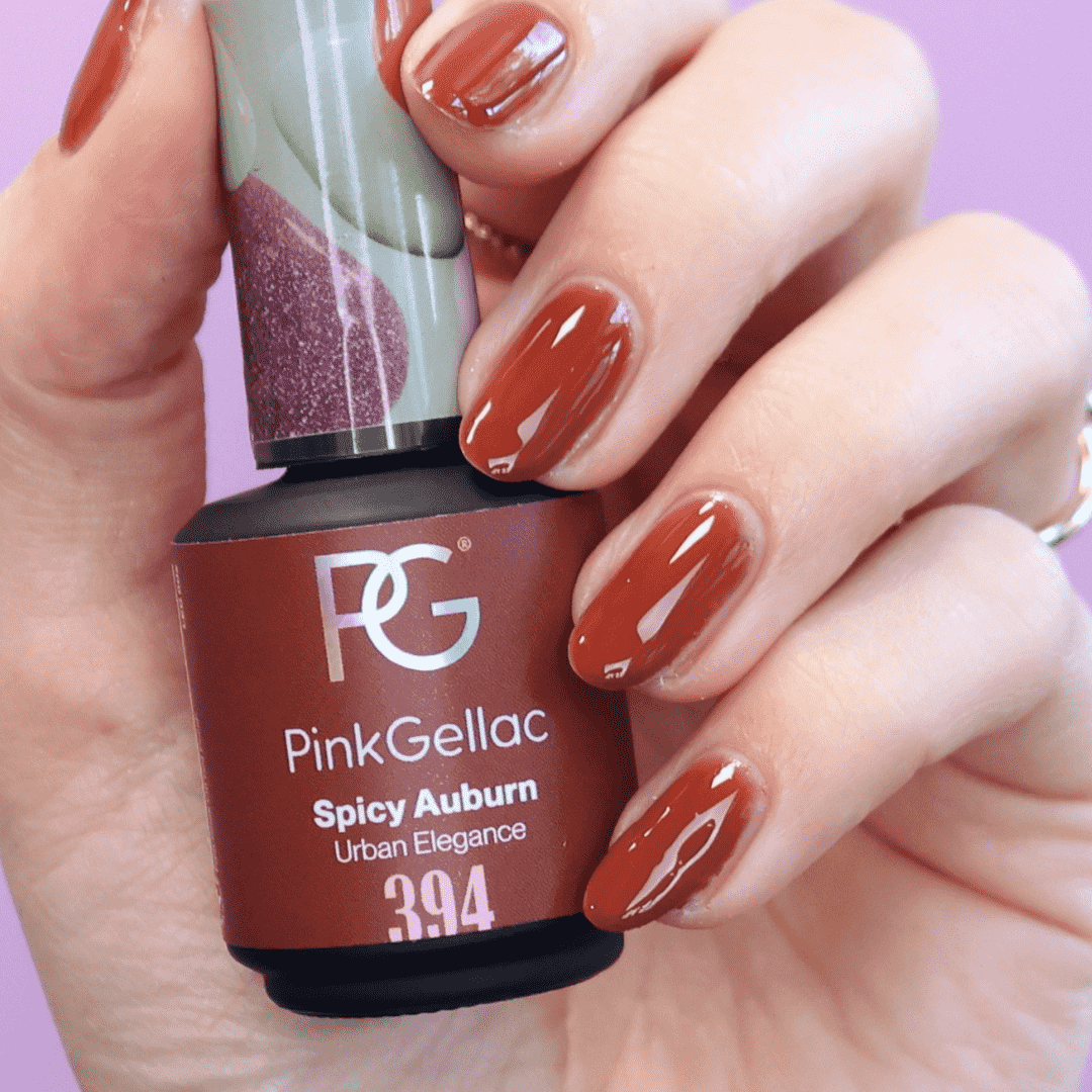 A hand with reddish-brown nail polish is holding a bottle of Pink Gellac with the color "Spicy Auburn".