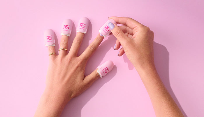One hand with pink nail protectors on each finger against a pink background, while the other hand removes a nail protector.