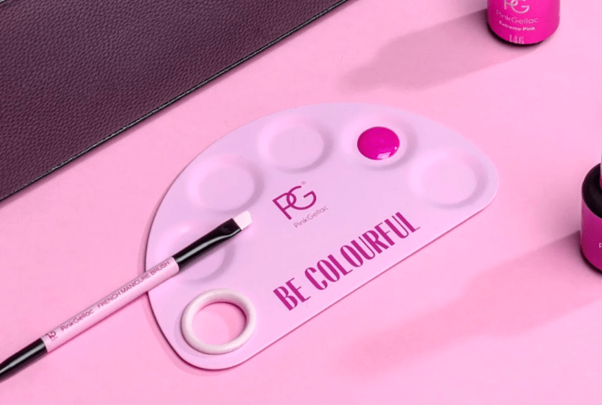 Pink nail polish palette with the text "Be Colorful", a brush and nail polish bottles on a pink background.