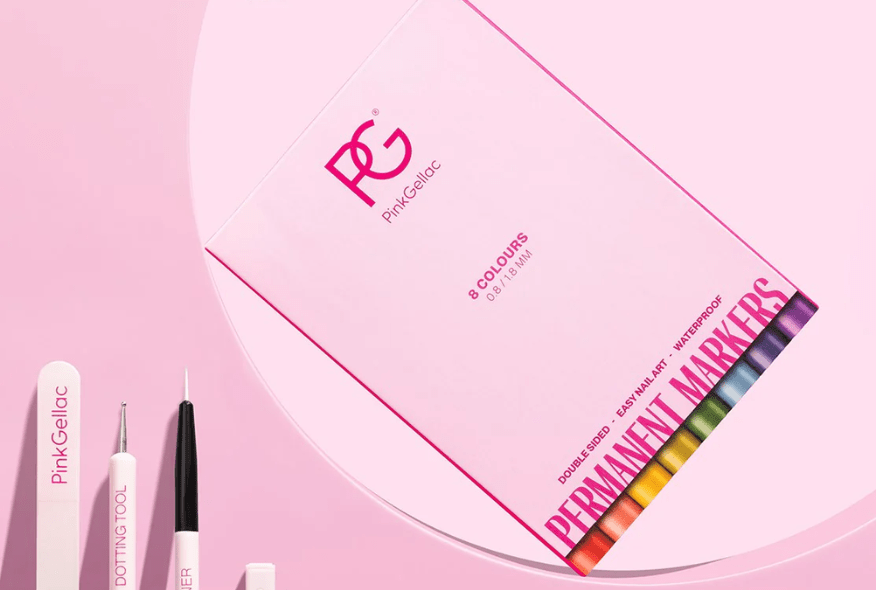 Close-up of Pink Gellac products on a pink background, including a box of permanent markers and nail tools such as a file, dotting tool and brush."