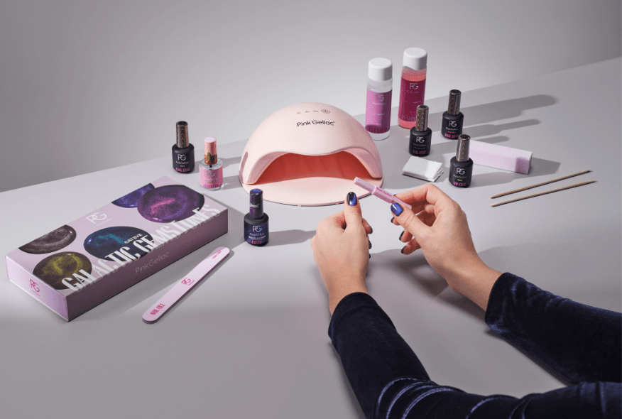 Person engaged in nail care, surrounded by gel polish products, a UV lamp and other accessories.