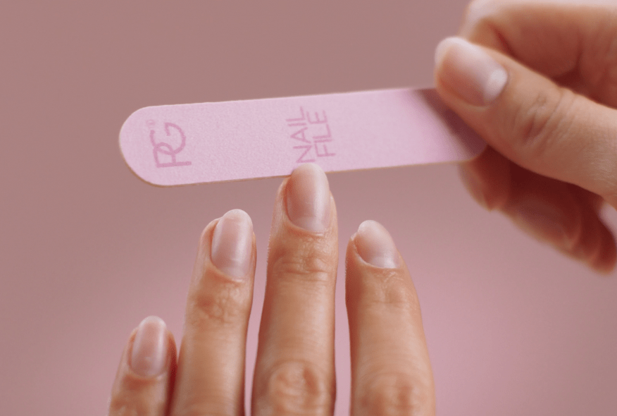 Close-up of a hand using a pink nail file on another hand with a pink background.