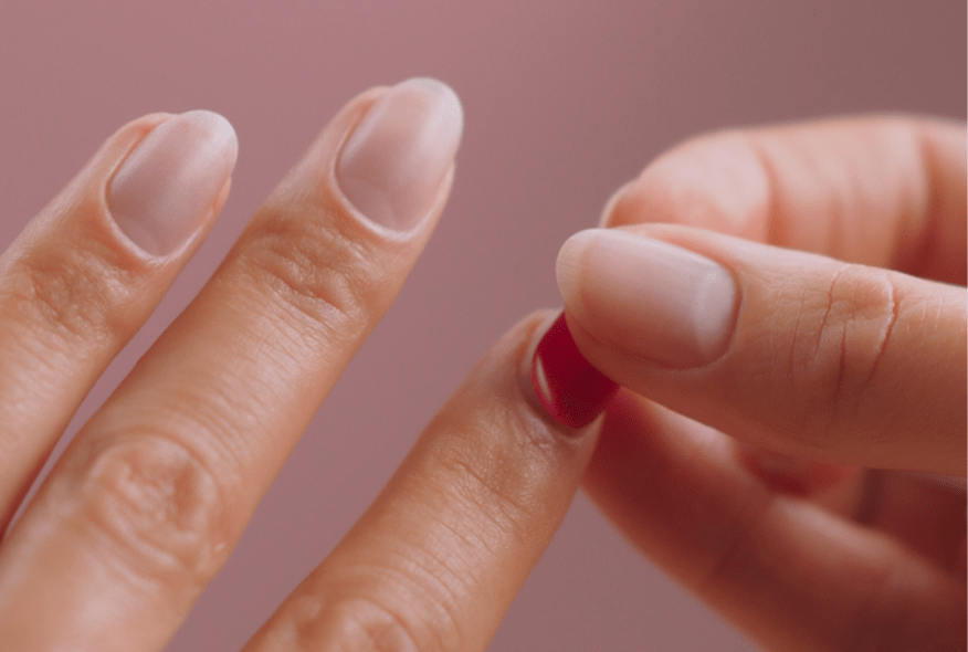 Two hands, one hand applying a red nail to the other hand against a pink background.