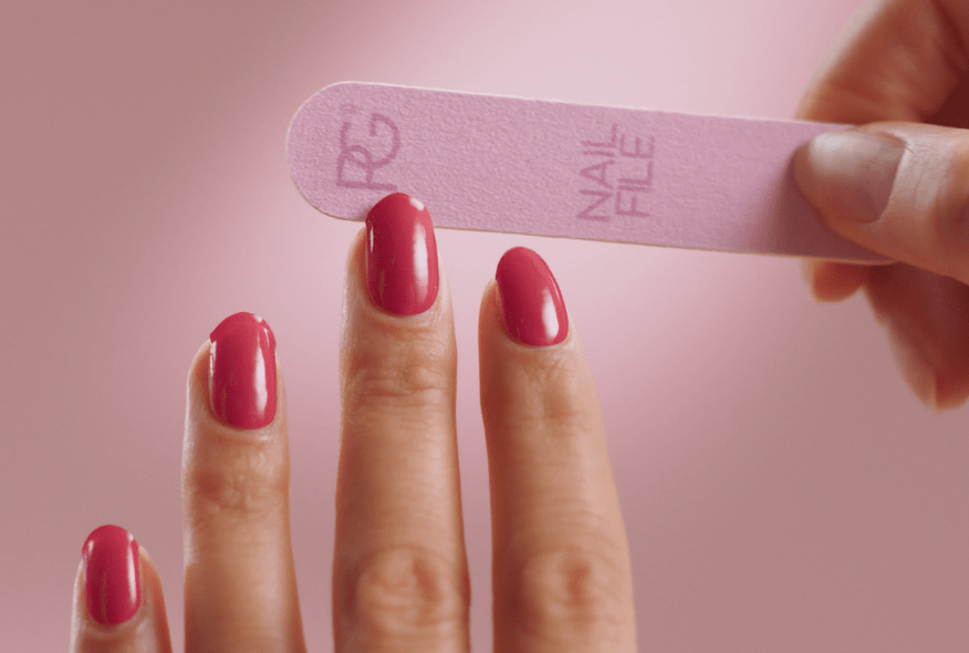 Person files pink painted nails with a pink nail file on a pink background.