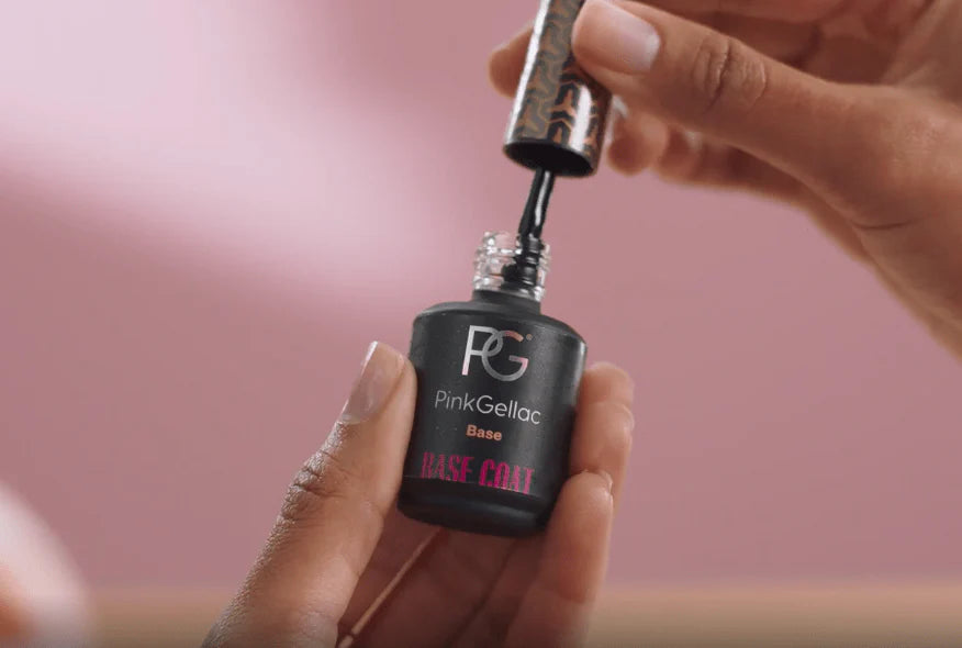 Hand holds a Pink Gellac Base Coat nail polish bottle against a pink background.