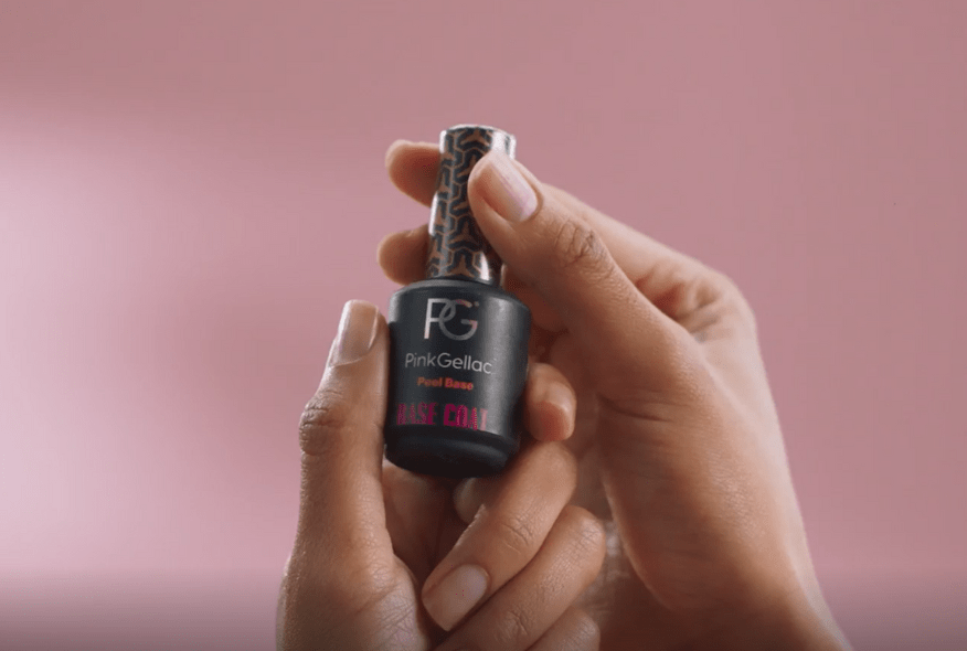 Two hands holding a bottle of Pink Gellac Peel Base against a pink background.