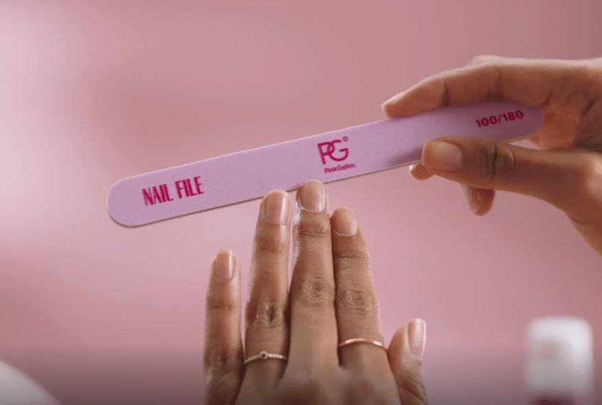 A close-up of hands using a pink PinkGellac brand nail file against a pink background.