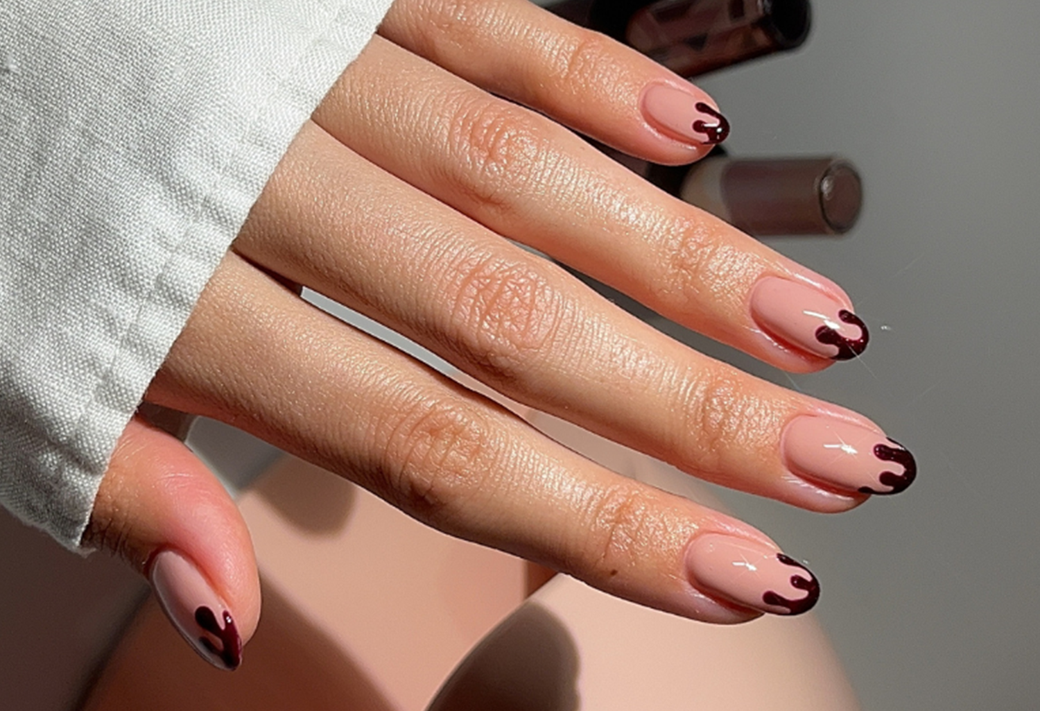 Hand holding nails in light shade with dark dripping nail art, over a white background.