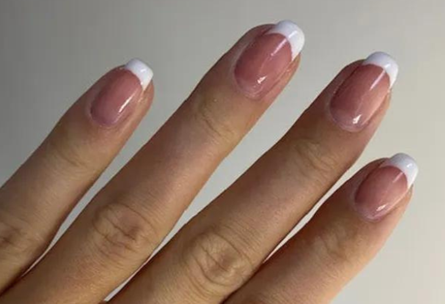 Four fingers with a French manicure, pink nails with white tips.