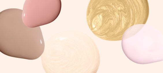 Different colors of nail polish drops on a light background, including pink, gold, beige and nude shades.