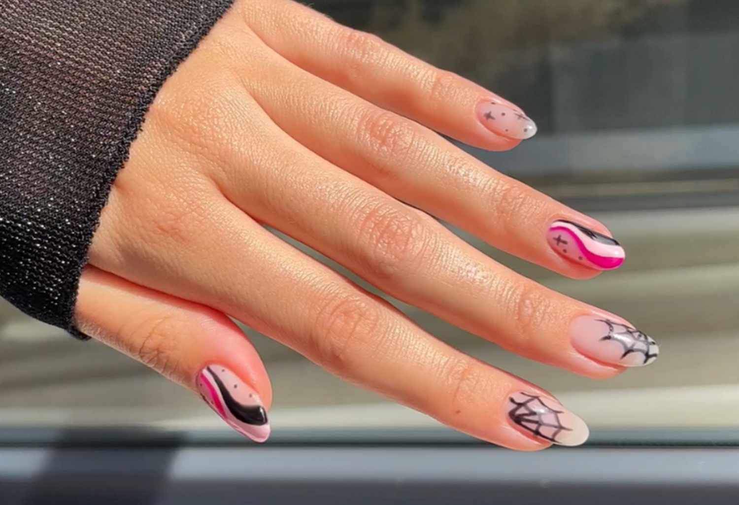 Hand with nails in artistic designs including pink and black lines and spider web patterns.
