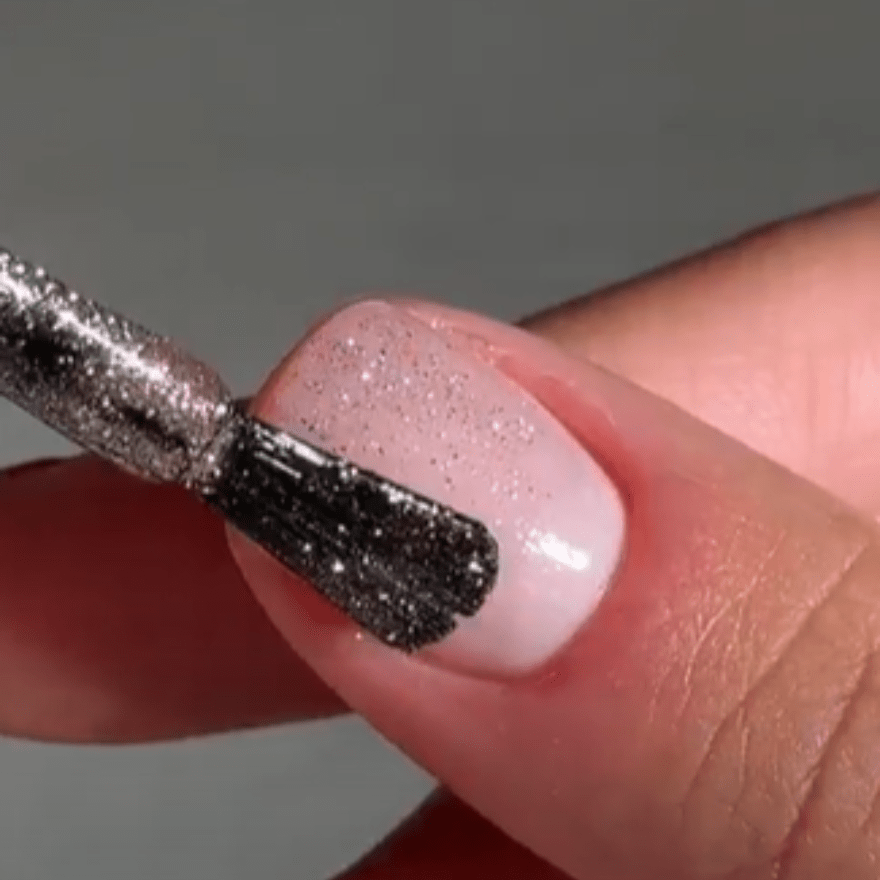 Close-up of a nail being painted with silver glitter nail polish.
