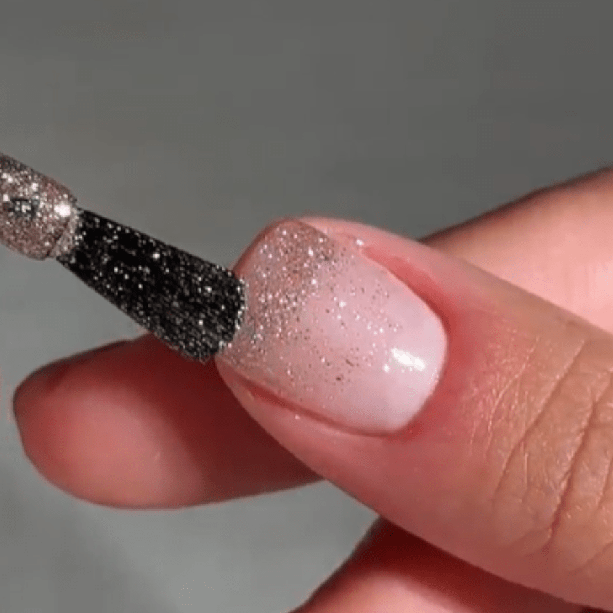 Close-up of a nail being painted with shiny silver glitter nail polish.
