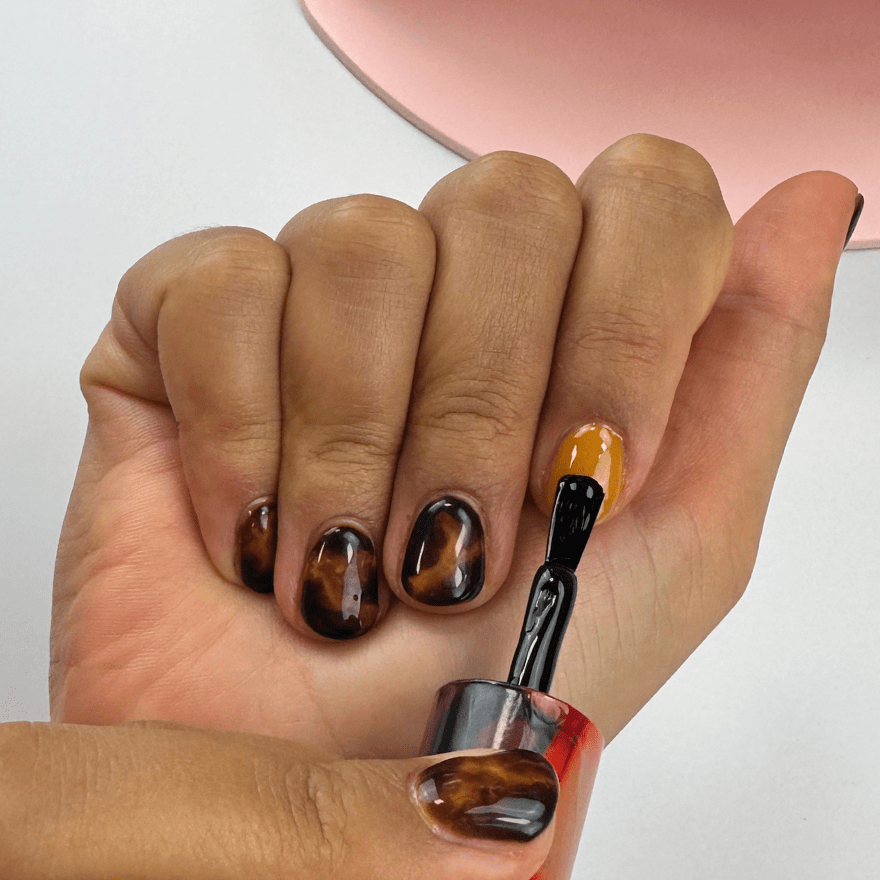 Hand with tortoiseshell pattern nail polish, where a nail is painted orange.