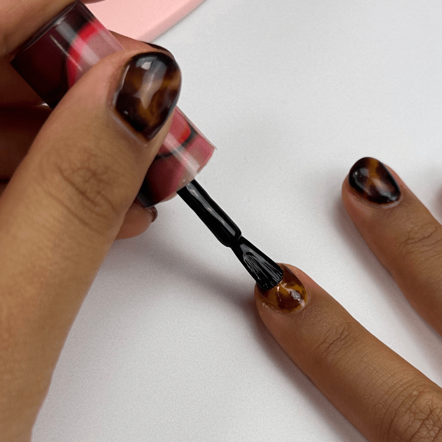 A person paints his nails with a dark nail polish, surrounded by a tortoiseshell pattern on a white background.