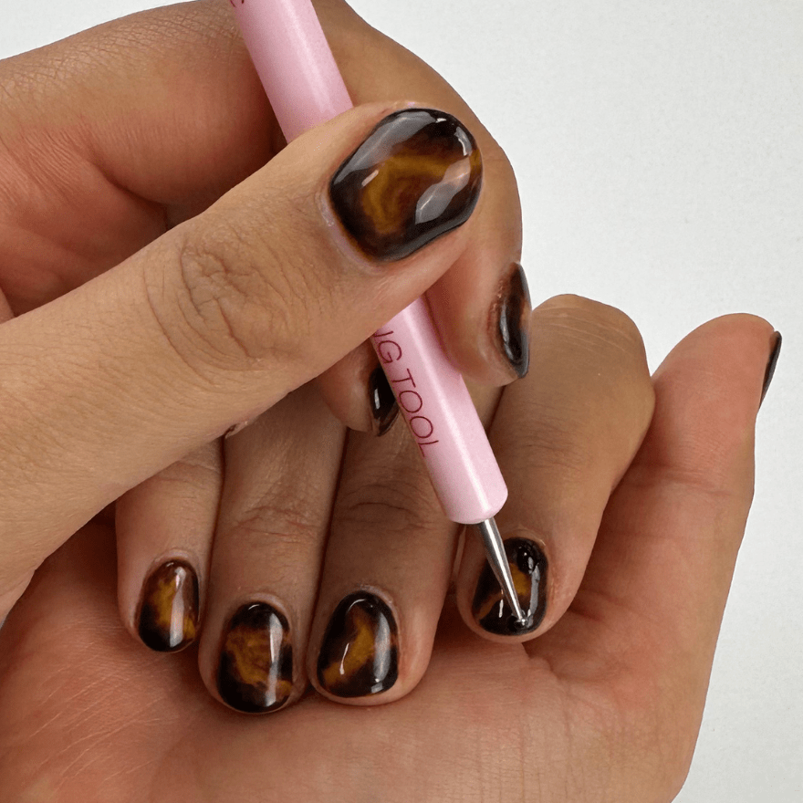 Person does nail art on short nails with a polished turtle pattern and uses a pink nail art tool.