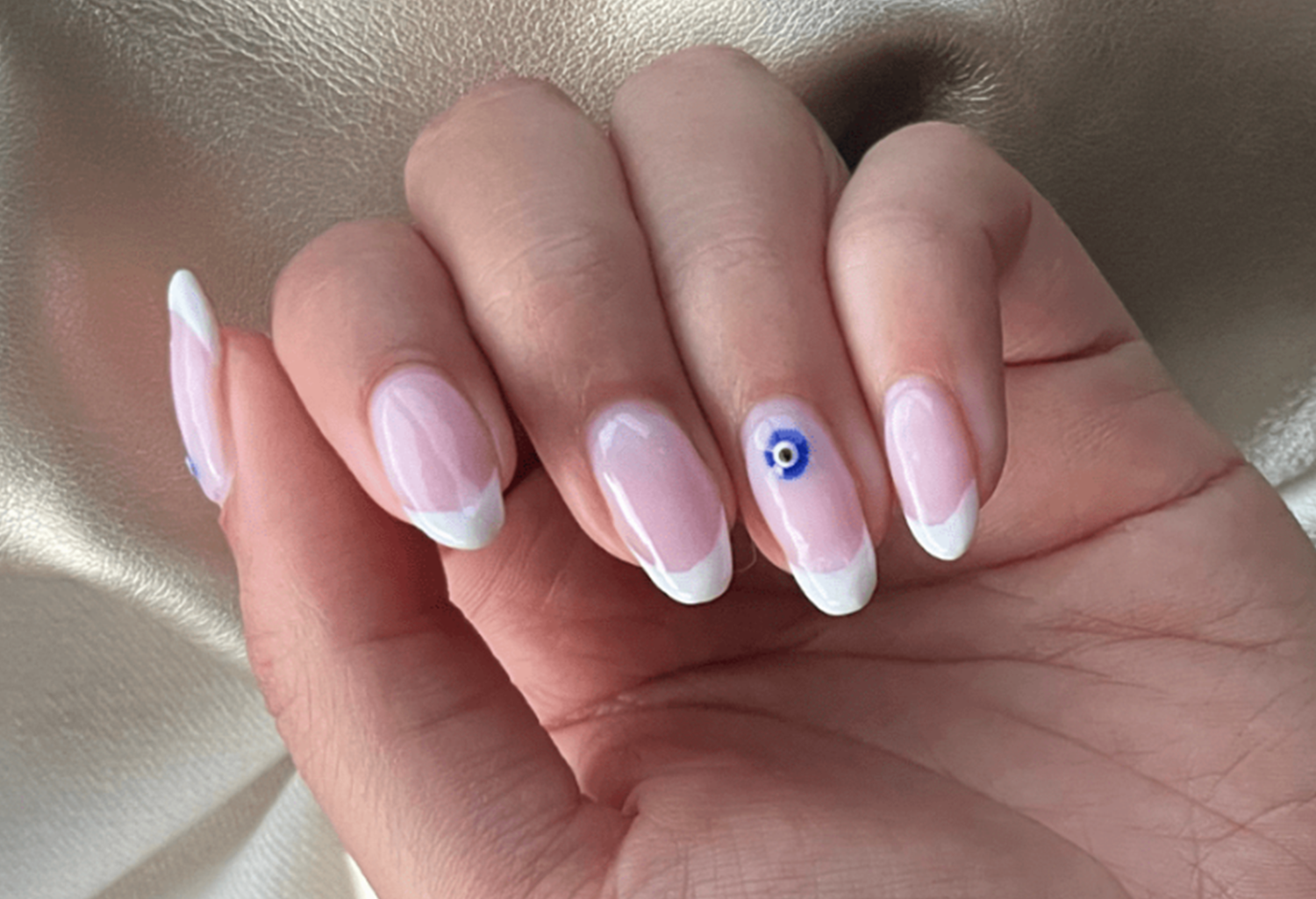 Hand with French manicure and a blue and white decoration on the ring fingernail, on a glossy background.