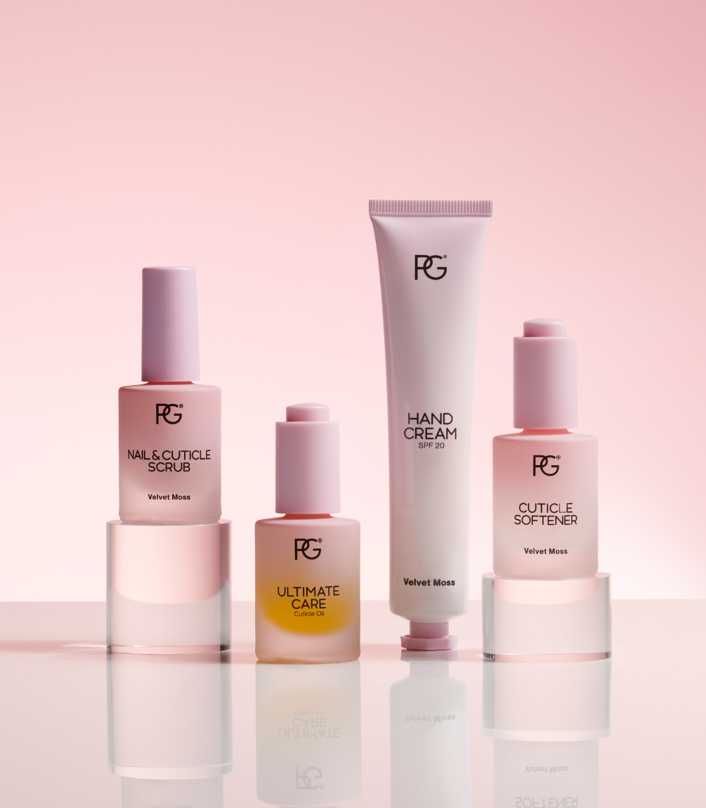 Four care products on a pink background, including nail and cuticle scrub, cuticle oil, hand cream and cuticle softener.