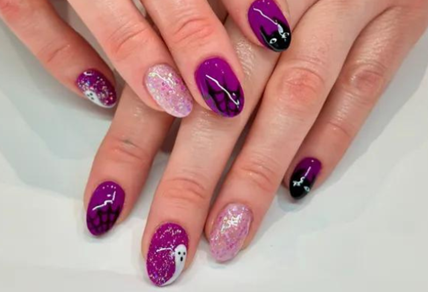 Purple nail art with glitter, spider webs and ghosts, suitable for Halloween.