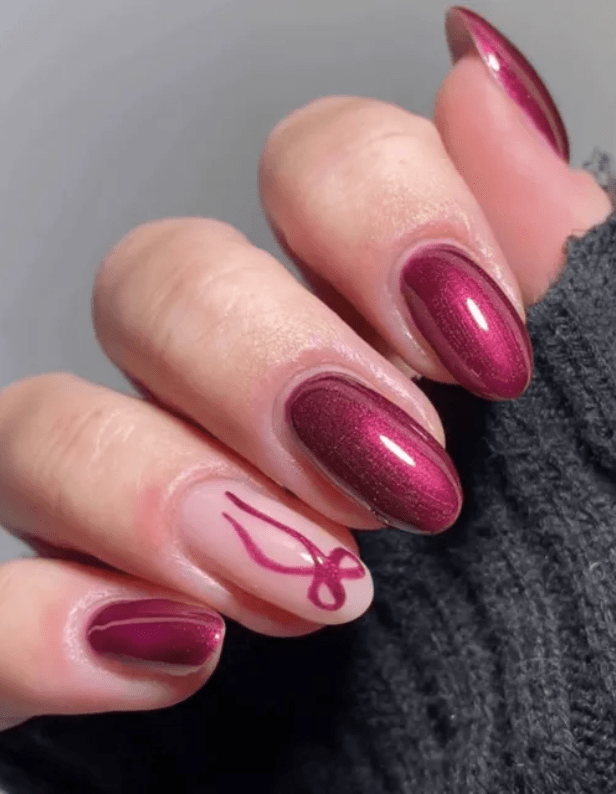 Hand holding dark pink nail polish, one©©nail has an abstract red line design, in a gray sleeve.