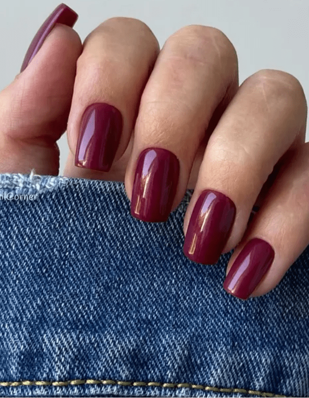 Hand with dark purple nail polish, resting on blue denim.