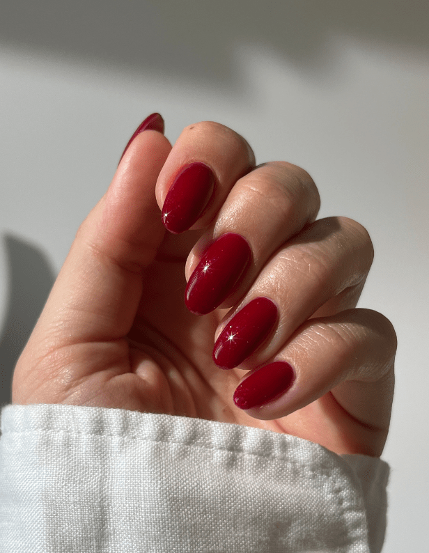 A hand with deep red painted nails, held in the light against a neutral background.