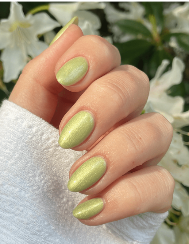 A hand with light green, shiny nail polish, in front of a background of white flowers.