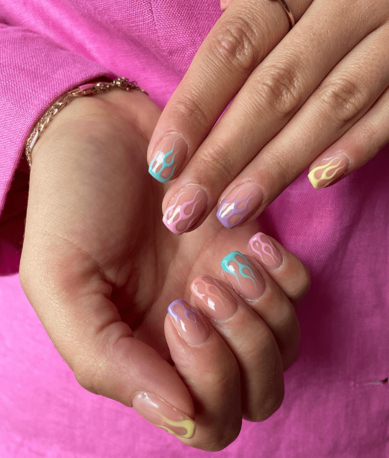 Close-up of hands with nails decorated with colorful flames on a pink background.