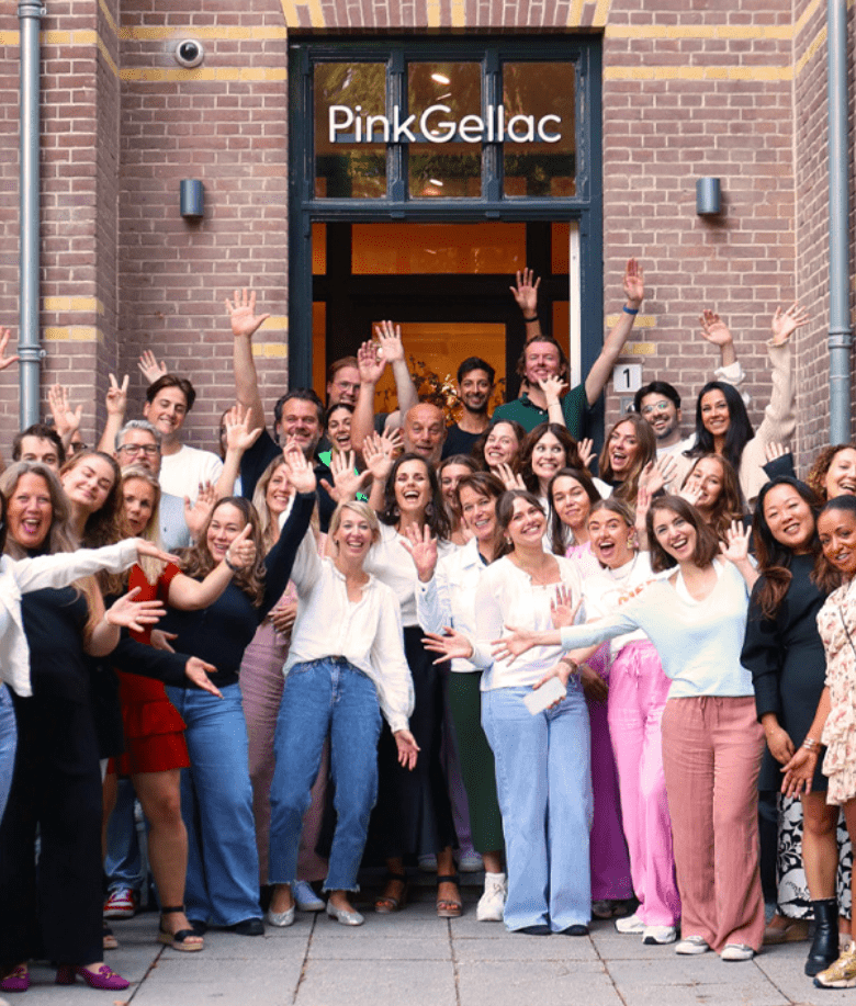 Group of people standing in front of a building with the Pink Gellac logo and waving happily at the camera.