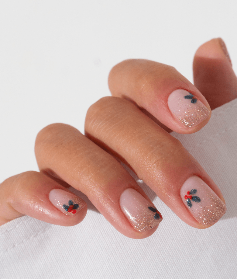 Hand with nude nail art, decorated with gold glitter and blue with red flower motifs.