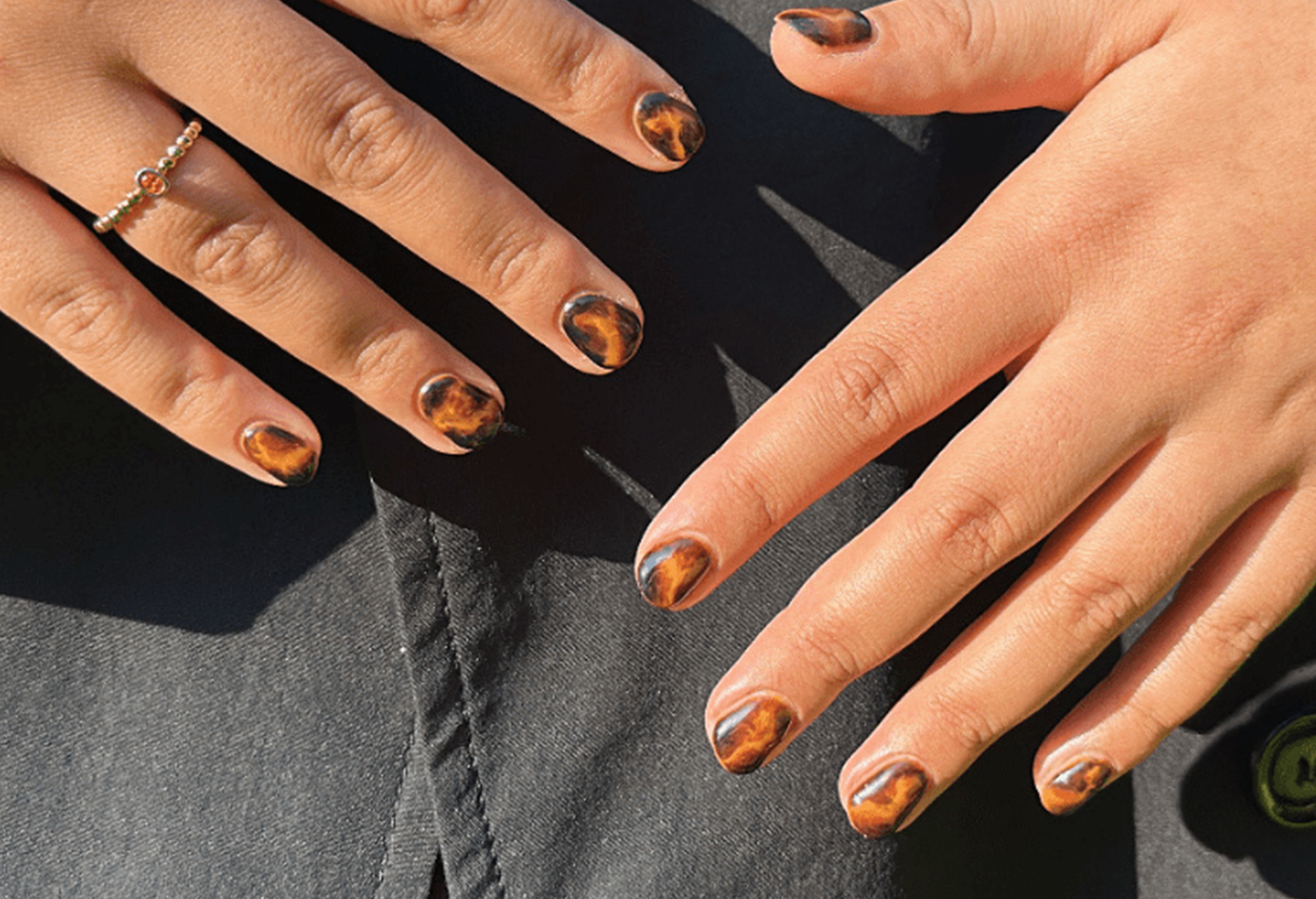 Hands with brown and black, marble-like nails; one hand wears a gold ring.