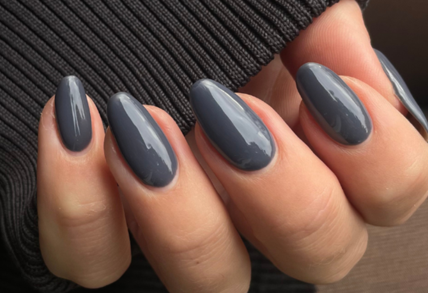 Hand holding dark gray painted nails on a black ribbed background.