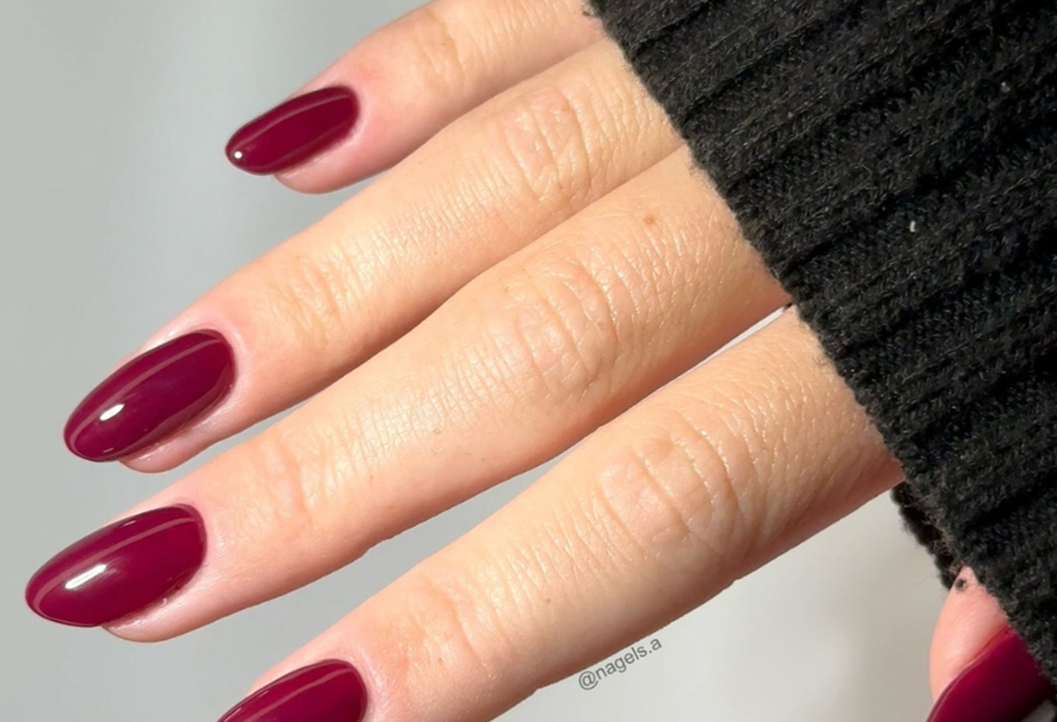 Close-up of a hand with dark red painted nails and a black sweater.