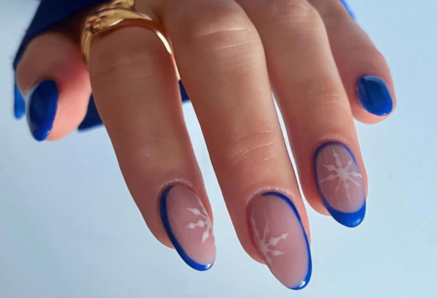 Close-up of a hand with blue painted nails and a white snowflake design on the middle nails.