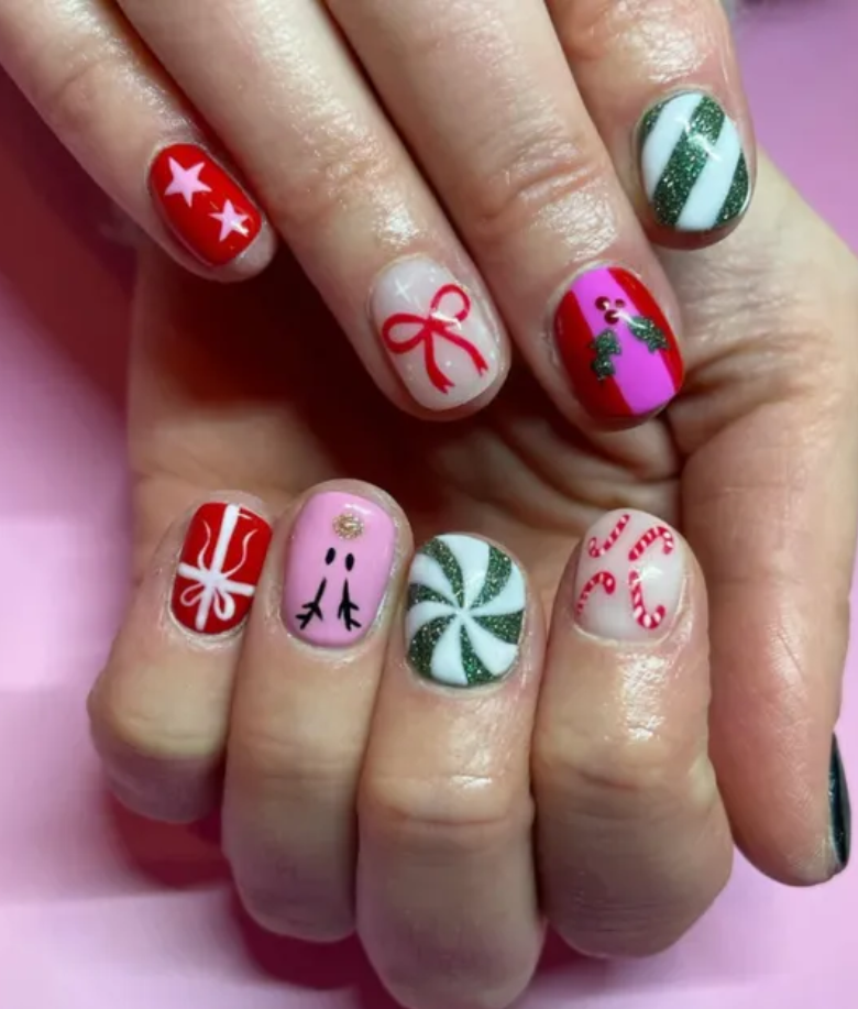 Hand with festive Christmas-themed nail art, including patterns of stars, bows, holly leaves, gift ribbons, a face, peppermint and candy canes.