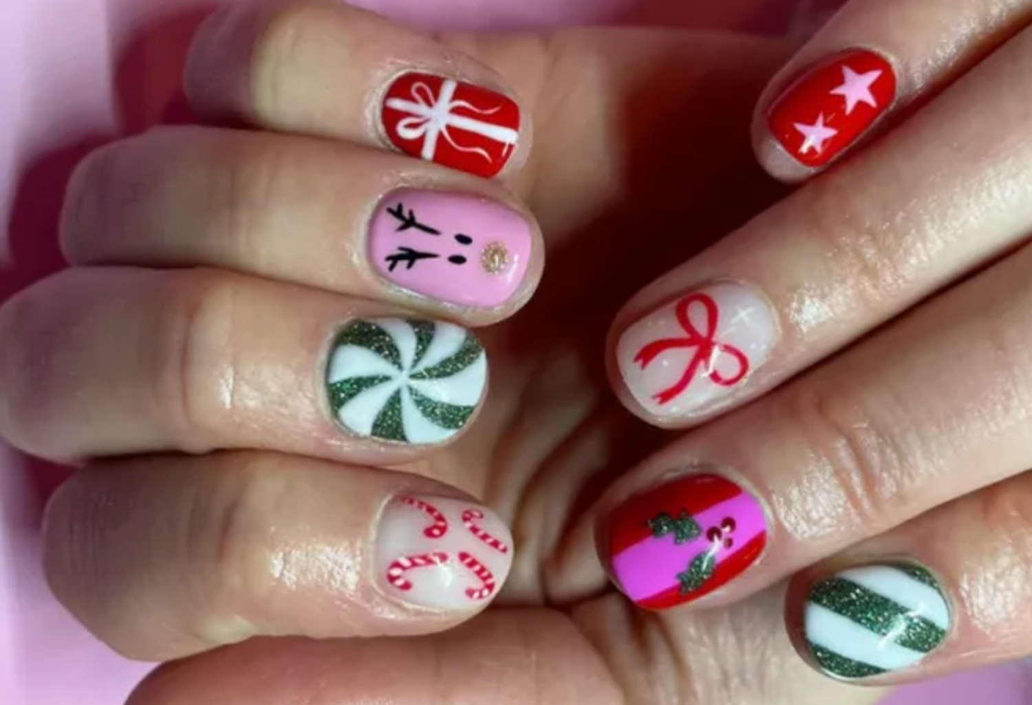 Colored Christmas-themed nails, including designs such as gifts, stars, a peppermint candy, holly leaves and a bow.