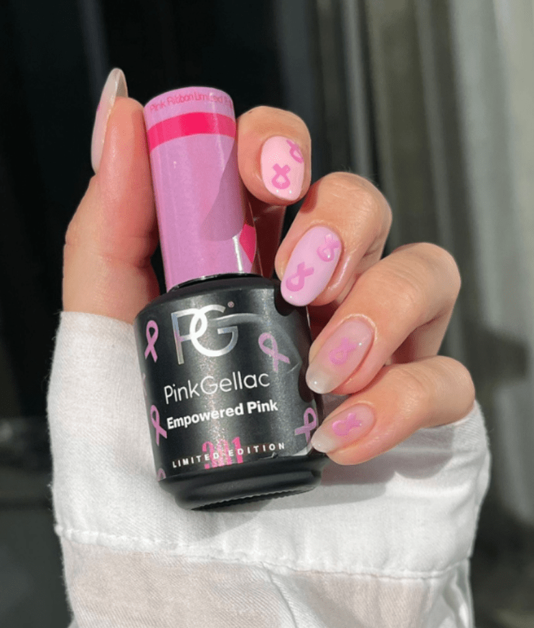 A hand with pink painted nails with pink ribbons, holding a bottle of Pink Gellac "Empowered Pink" gel nail polish.