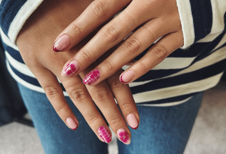 Hands with pink and red nail designs, including patterns and flowers, on a striped sweater background.