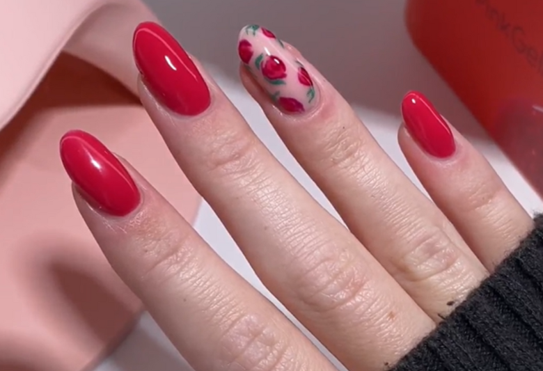 Hand with long, red painted nails and a ring finger with rose pattern.