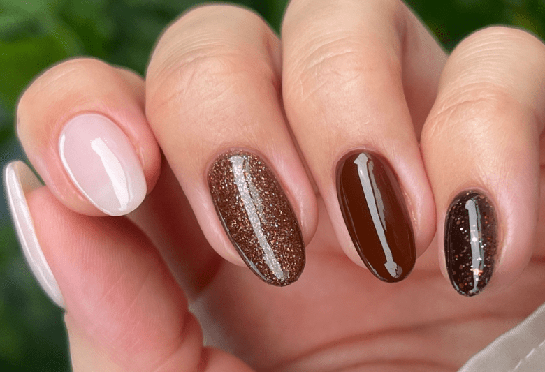 Close-up of a hand with five nails painted in various shades of brown, including shiny and shimmering finishes.