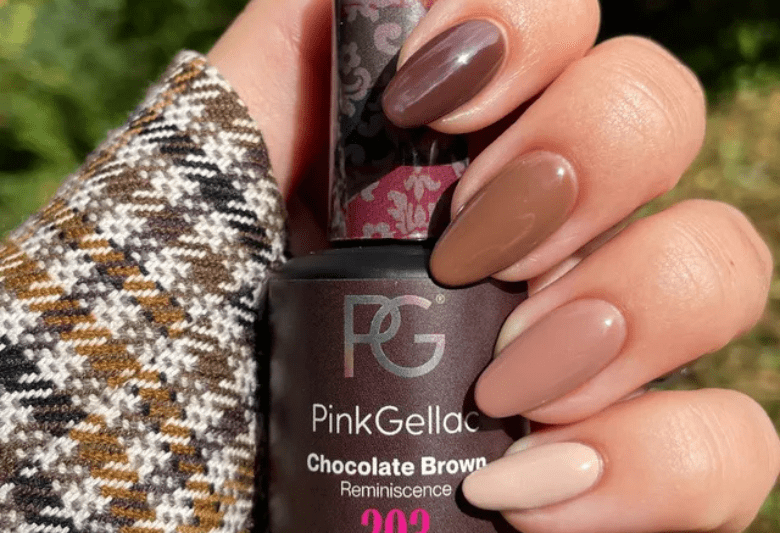 Close-up of a hand holding different shades of brown nail polish, holding a bottle of Pink Gellac Chocolate Brown nail polish, against a background of a checkered fabric.