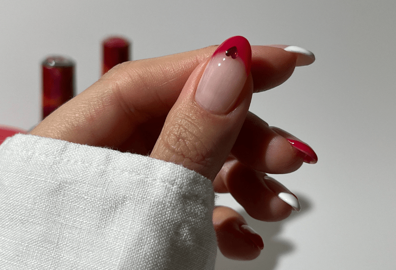 Close-up of a hand with red and white painted nails, with a heart on the thumbnail, wrapped in a white sleeve.